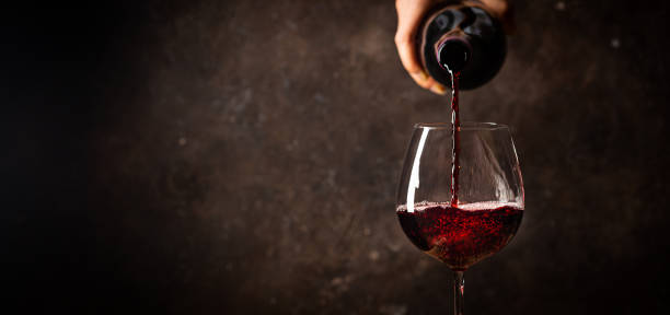 Pouring red wine into the glass against rustic dark wooden background